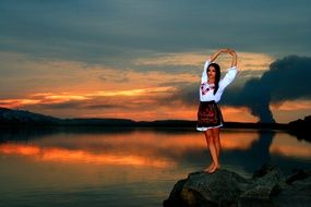 girl in a Ukrainian costume stands on a stone at sunset