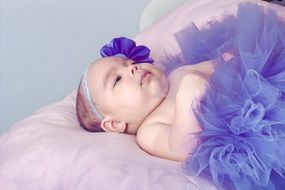 baby Girl in purple clothe lays down on her back