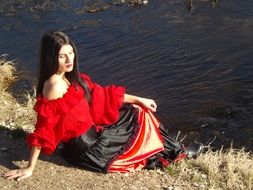 gypsy woman in a red-black dress near the water