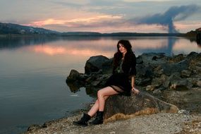 girl in a black dress near the water at sunset