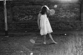 child Girl in white Dress stays on pavement at wall