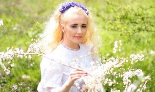 blonde in a wreath with blue flowers among nature