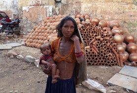 young Mother with baby at pile of clay pots outdoor, Poverty, India