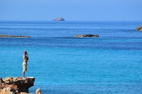 pensive man on a cliff above the water in ibiza