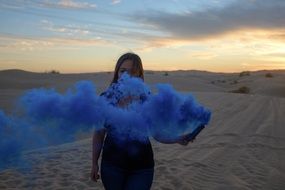girl among sand dunes with blue smoke