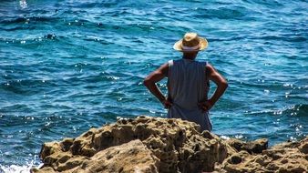 old man stands on a rock and looks at the sea