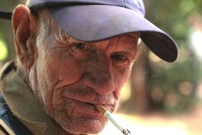 old man in a cap smokes close-up on blurred background