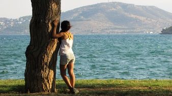 girl stands by a lonely tree by the sea