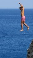 man jumping into the sea from the rock on a sunny day