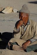 an elderly man sits on the bare ground in Tibet