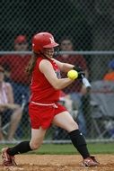 Swinging girl in red uniform, playing Softball on the field