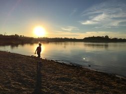 a child walks along the shore of Lake Folsom at dusk