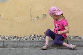 little girl in colorful clothing with stones near the house