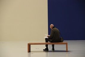 man with a book on a bench near the blue wall