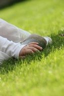 child holds leg while sitting on green grass