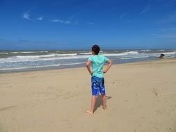 boy in blue clothes stands on a sandy beach