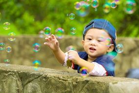 happy child among the colorful soap bubbles in the park with plants