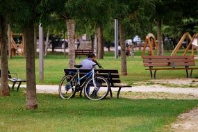 a man sits on a park bench next to a bicycle