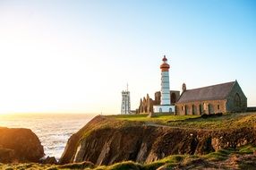 a lighthouse stands near a church on a hill