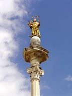 Golden statue of catholic church at blue sky background with white clouds