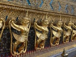 golden fantasy sculptures in row at wall, Thailand, Bangkok