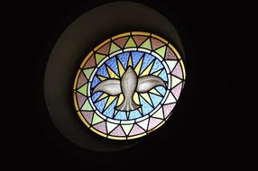 holy spirit as dove, round stain glass window in darkness