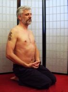 Relaxed meditating man with bare torso and tattoo