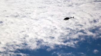 helicopter flies under white clouds