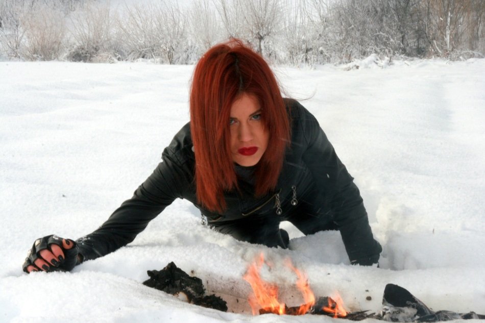 beautiful girl with red hair near a fire in the snow