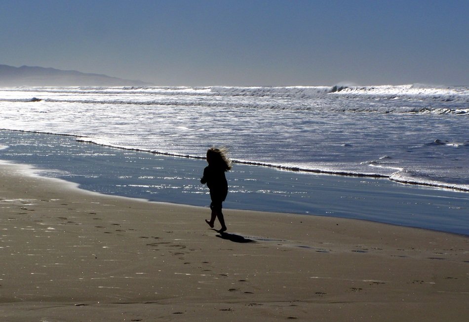 the child walks along the sandy coast against the backdrop of the sea waves