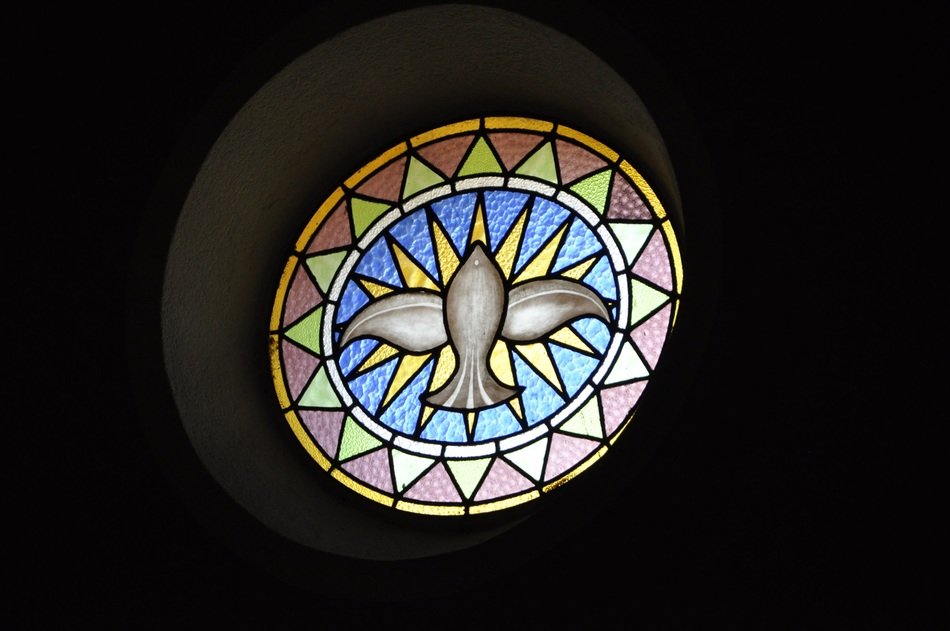 holy spirit as dove, round stain glass window in darkness