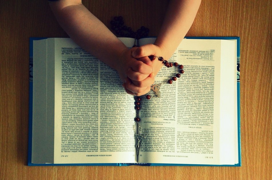 Praying personâs hands with Rosary on open Bible
