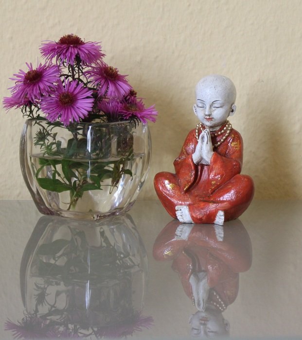 figurine of a little buddha and flowers on a glass table