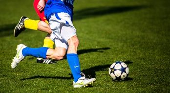 photo of soccer players legs and ball on the lawn