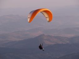 athlete with an orange parachute flying over the mountains on beautiful landscape