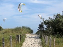 paragliding wings in sky above sand dune