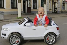 happy child boy in white toy car on street