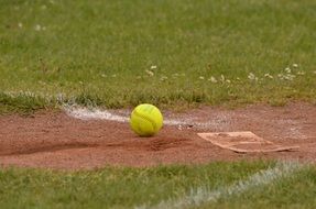 yellow Softball ball on red Gravel at Grass