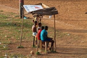 black children sit under a makeshift canopy and watch a football match