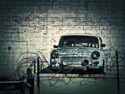 old car behind barbed wire against a brick wall