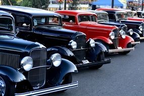 multi-colored vintage cars stand in a line in a parking lot