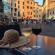 two glasses and a hat on a table in a street cafe in Rome