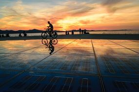 cyclist rides along the promenade in Zadar at colorful sunset in sky