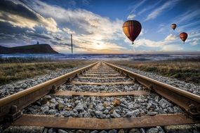 Hot Air Balloons in sunset Sky above railway on the landscape and water on the horizon