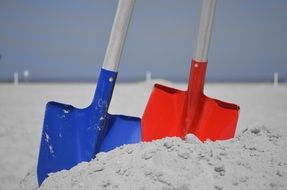 red and blue shovels in the sand