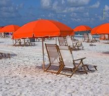 orange umbrellas and chairs on white sand at the beach