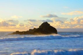 foamy Waves in front of scenic Rock in Ocean at evening