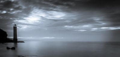 black and white photo of a lighthouse on the ocean against a gray sky
