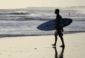 man with a surfboard walks along the beach