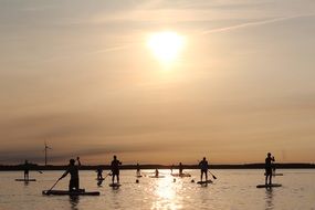 people stand on surfboards with oars on the water